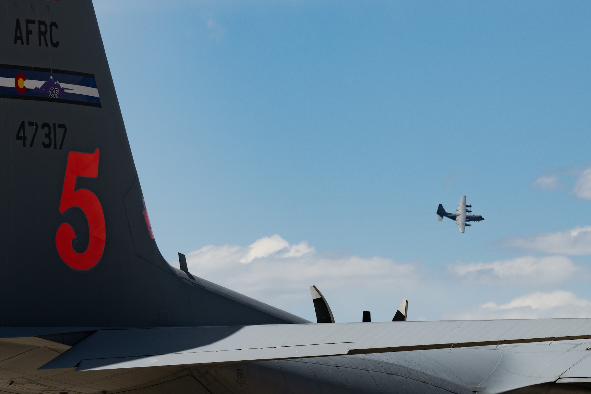 An aircraft tail with the number "5" on it and an aircraft flying in the background.