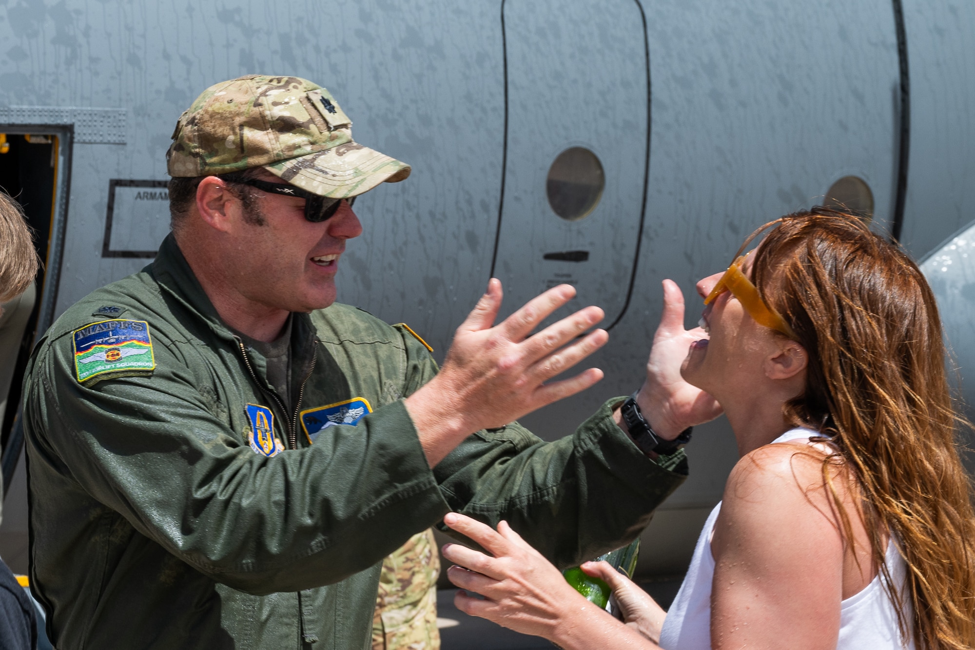 A man in a flight suit holding his hands up to embrace his wife.