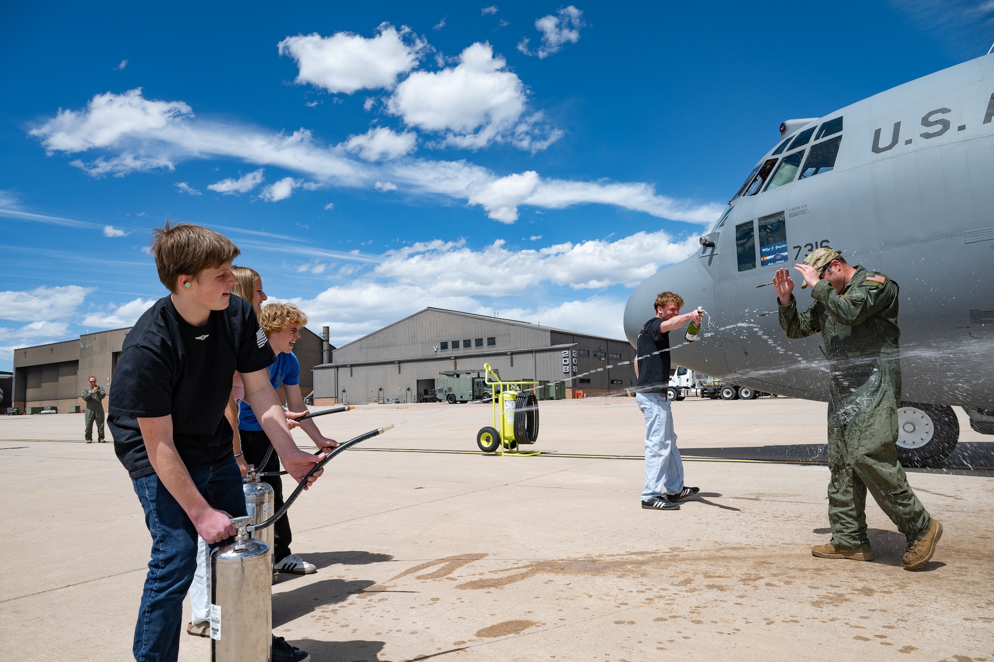 Children douse their father with water in front of a military aircraft.