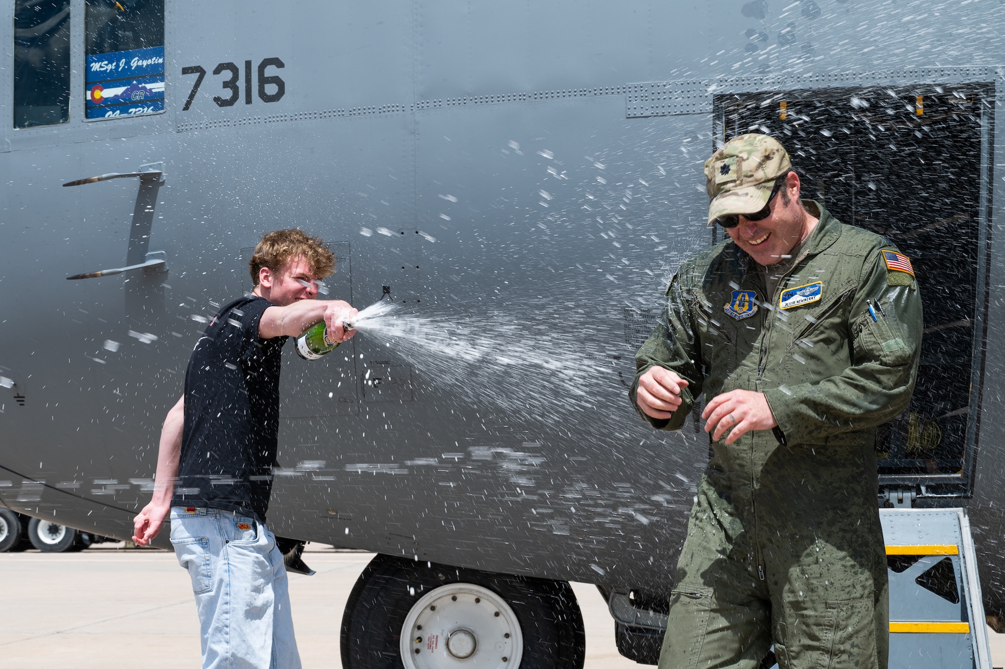 A man in a flight suit is sprayed in front of an aircraft.