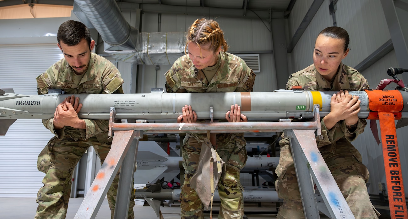 Three Airmen transfer an AIM-9X missile to a stand.