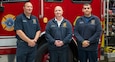 Three people wearing Tobyhanna Army Depot Fire & Emergency Services apparel stand in front of a firetruck and pose for a photo.