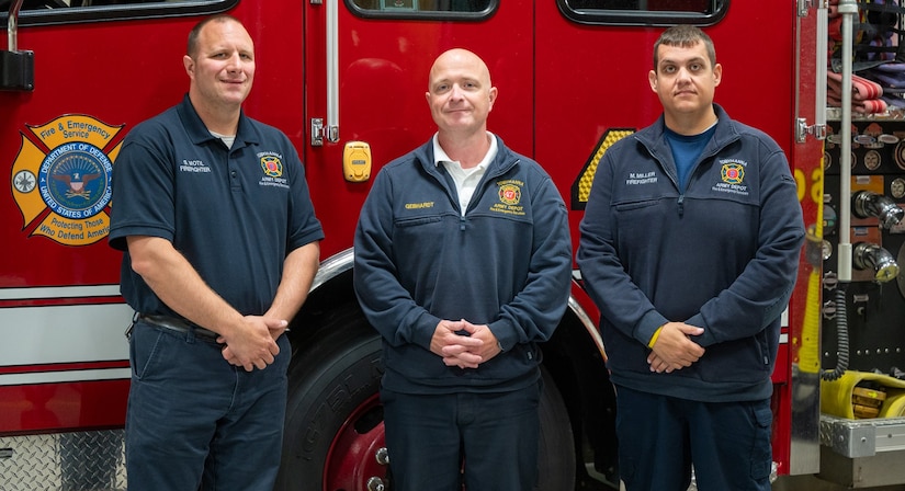 Three people wearing Tobyhanna Army Depot Fire & Emergency Services apparel stand in front of a firetruck and pose for a photo.