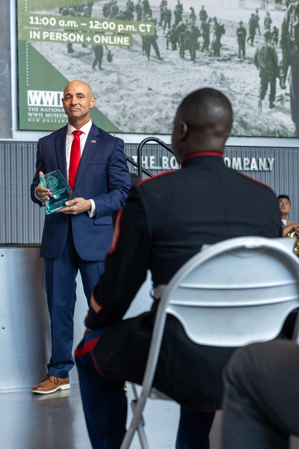 Retired U.S. Marine Corps Col. Jason E. Burkett, prepares to hand U.S. Marine Corps Sgt. Isaiah J. Curtis, color sergeant, Marine Forces Reserve and Marine Forces South, the Mayor of New Orleans Commendation Award during the Armed Forces Day award ceremony at the National WWII Museum, May 17, 2025. Curtis was awarded for his dedication and service to the local community, having rendered colors for over 250 organizations in the greater New Orleans area. Curtis actively participates in volunteer events across New Orleans including Habitat for Humanity, which assists in the construction of homes in the lower ninth ward. He also volunteers with Culture Aid NOLA, which distributes food aid to members of the New Orleans community.   (U.S. Marine Corps photo by Cpl. Kanoa Thomas)