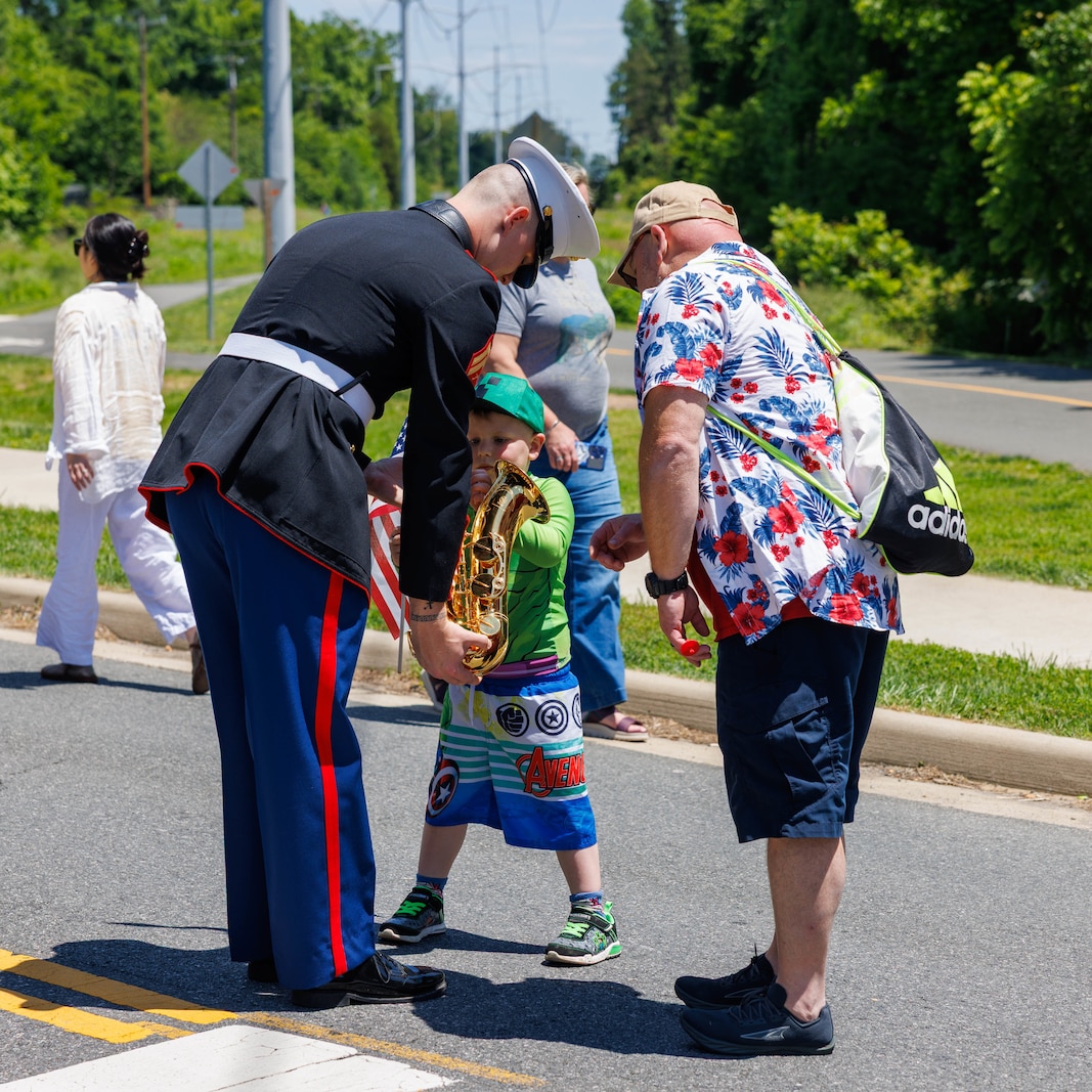 A U.S. Marine with the Quantico Marine Band shows an instrument to crowd members during the Memorial Day parade in the City of Falls Church, Virginia, May 26, 2025.  The City of Falls Church Memorial Day Parade is an annual event that honors the service members who have made the ultimate sacrifice.  (U.S. Marine Corps photo by Lance Cpl. Donovan E. Melendez)