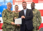 Ricky McNaron, NSWC PCD Mine Countermeasures (MCM) Unmanned Surface Vehicle and Payload Delivery System program manager, receives recognition from (then) Rear Adm. Casey Moton, Program Executive Office, Unmanned and Small Combatants (PEO USC) program executive officer, April 24, 2023. The Navy’s Littoral Combat Ship MCM mission package and AN/AQS-20 Sonar Mine Detection Sets achieved initial operational capability. (left to right in back) Capt. David Back, (then) NSWC PCD commanding officer, and Capt. Gus Weekes, program manager Littoral Combat Ship Mission Modules were also present. (U.S. Navy photo by Eddie Green)