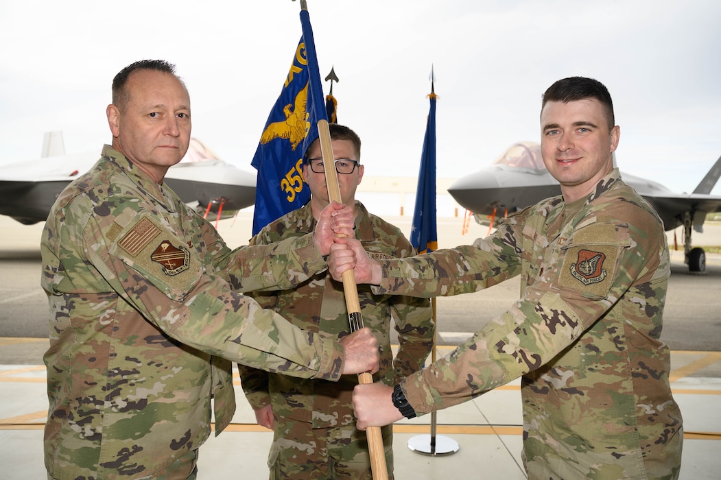 U.S. Air Force Col. Jerry Copeland, left, 354th Maintenance Group commander, passes the 356th Fighter Generation Squadron guidon to Maj. Matthew Ward, incoming 356th Fighter Generation Squadron commander, during a change of command ceremony