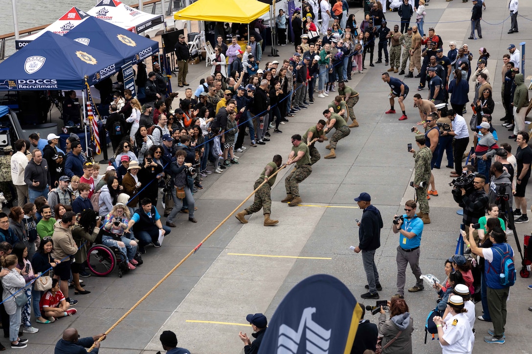 Groups of service members and civilians pull on a rope while a crowd watches.