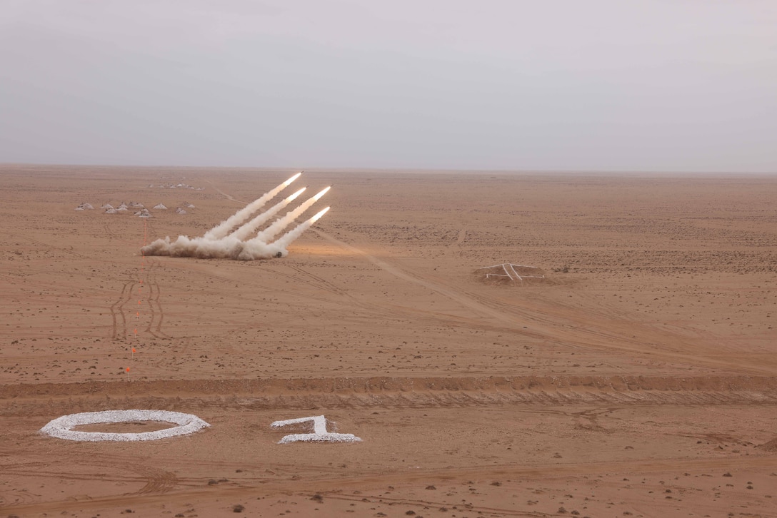 Four rockets launch in a desert environment under cloudy skies.