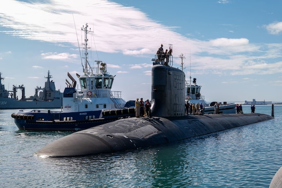 Close up of stationary submarine in water with a boat on its left.