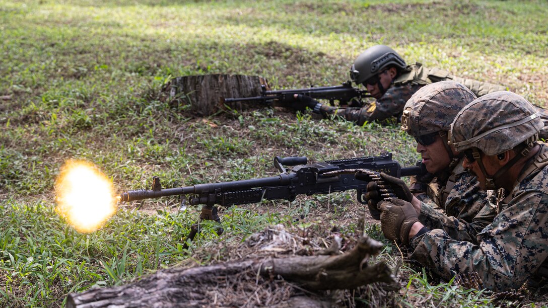 Two U.S. service members and one Guatemalan service member lay on the grass with guns