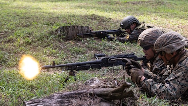 Two U.S. service members and one Guatemalan service member lay on the grass with guns