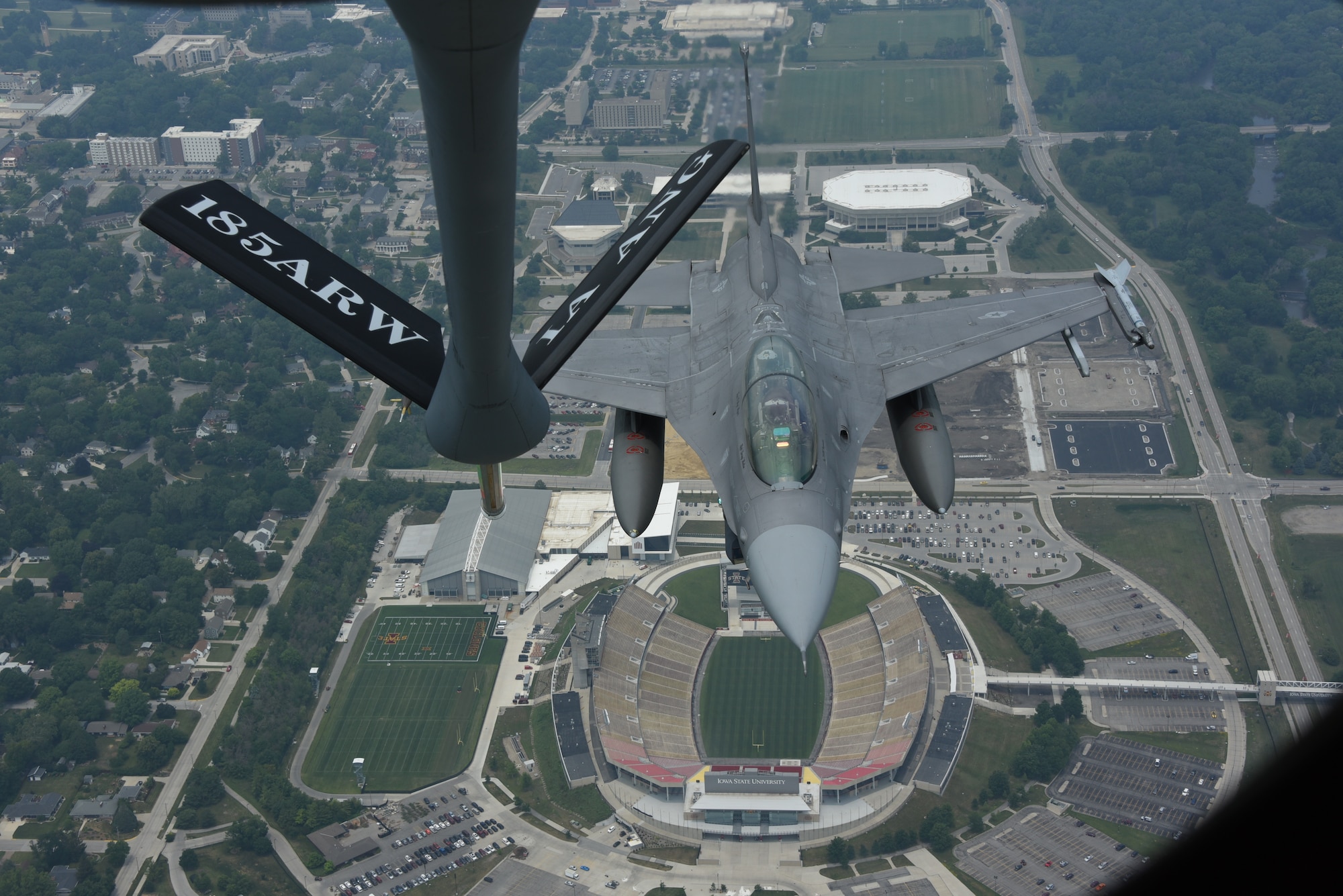 A refueling boom hangs over an F-16 fighter jet as it flies over Jack Trice Stadium