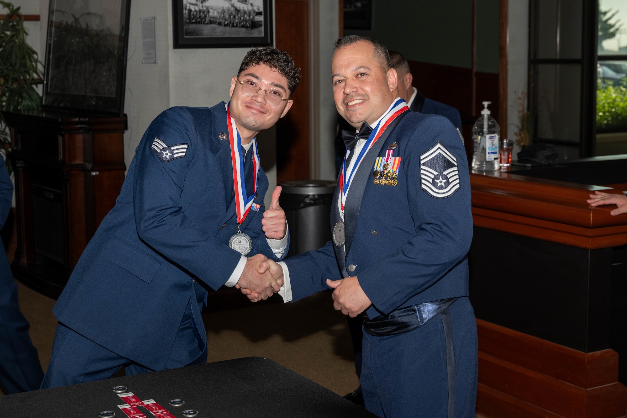 Two Airmen pose during the CMSAF Thomas N. Barnes Airman Leadership School Class 25-D Medallion Ceremony.