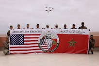 U.S. Marines and Soldiers from the Royal Moroccan Armed Forces pose for a group photo while F16 fighter jets pass overhead at Cap Draa during African Lion 25 (AL25) in Tan-Tan, Morocco, May 23, 2025. AL25, the largest annual military exercise in Africa, brings together over 50 nations, including seven NATO allies and 10,000 troops to conduct realistic, dynamic and collaborative training in an austere environment that intersects multiple geographic and functional combatant commands. Led by U.S. Army Southern European Task Force, Africa (SETAF-AF) on behalf of the U.S. Africa Command, AL25 takes place from April 14 to May 23, 2025, across Ghana, Morocco, Senegal, and Tunisia. This large-scale exercise will enhance our ability to work together in complex, multi-domain operations—preparing forces to deploy, fight and win.