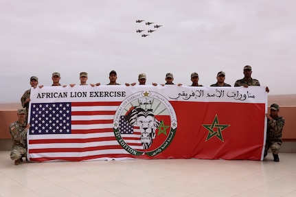 U.S. Marines and Soldiers from the Royal Moroccan Armed Forces pose for a group photo while F16 fighter jets pass overhead at Cap Draa during African Lion 25 (AL25) in Tan-Tan, Morocco, May 23, 2025. AL25, the largest annual military exercise in Africa, brings together over 50 nations, including seven NATO allies and 10,000 troops to conduct realistic, dynamic and collaborative training in an austere environment that intersects multiple geographic and functional combatant commands. Led by U.S. Army Southern European Task Force, Africa (SETAF-AF) on behalf of the U.S. Africa Command, AL25 takes place from April 14 to May 23, 2025, across Ghana, Morocco, Senegal, and Tunisia. This large-scale exercise will enhance our ability to work together in complex, multi-domain operations—preparing forces to deploy, fight and win.