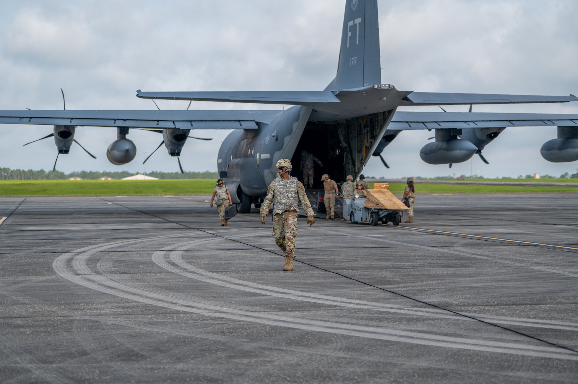 Man in the foreground walks away from plane in the background, as people unload it.
