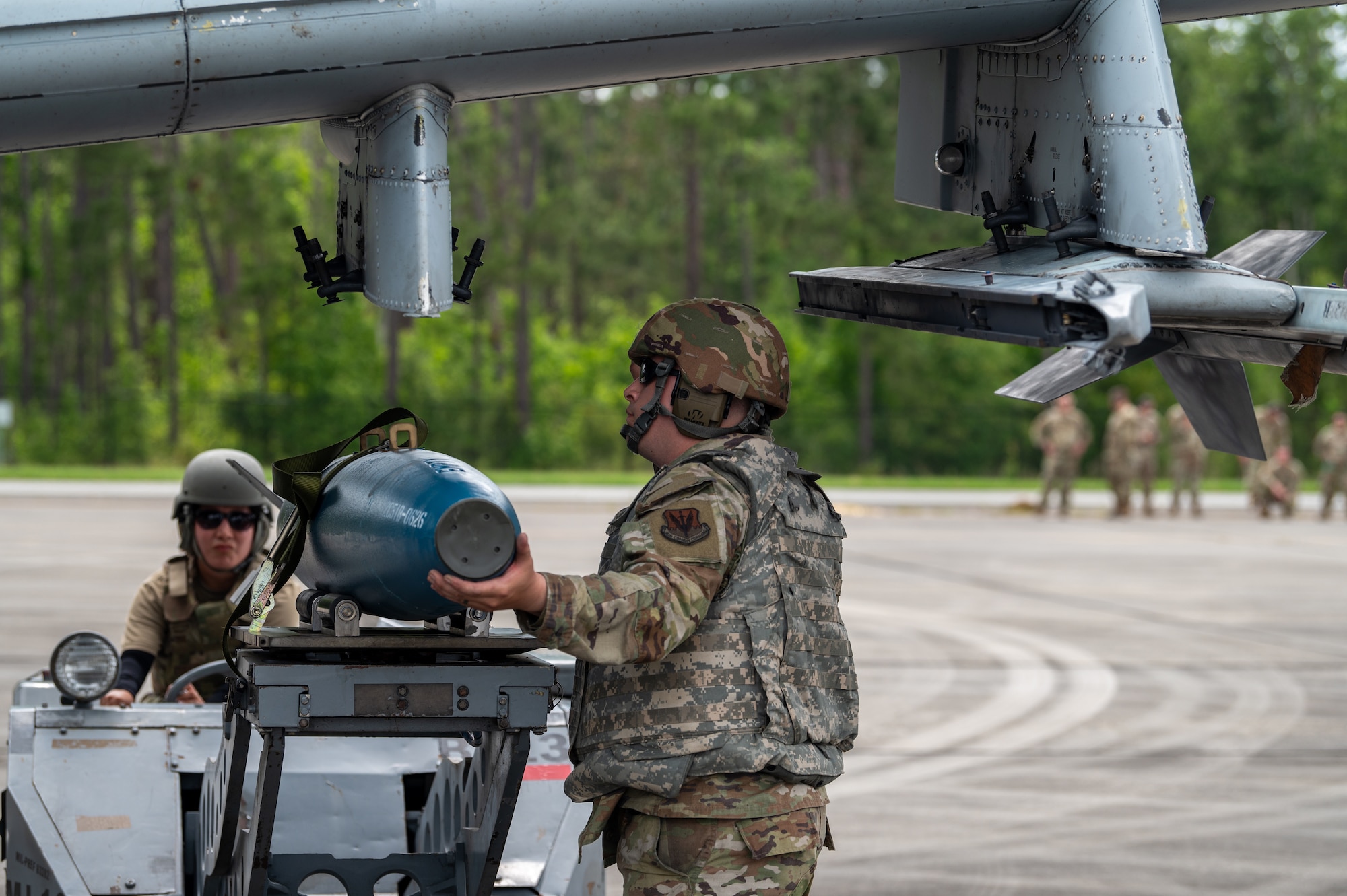 Two people are under a plane, loading practice bombs on it.