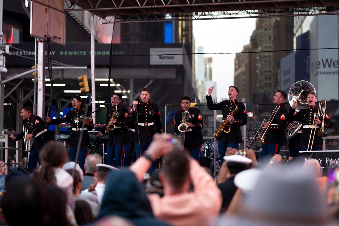 Marine Corps musicians perform for a large crowd outdoors in a city.