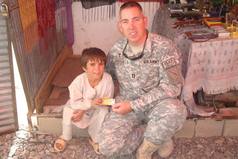 Chaplain (Cpt.) William Draper takes a photo with an Afghan child while he was visiting a local bazar during his deployment to Afghanistan with the 201st Engineer Battalion in 2008-2009.
