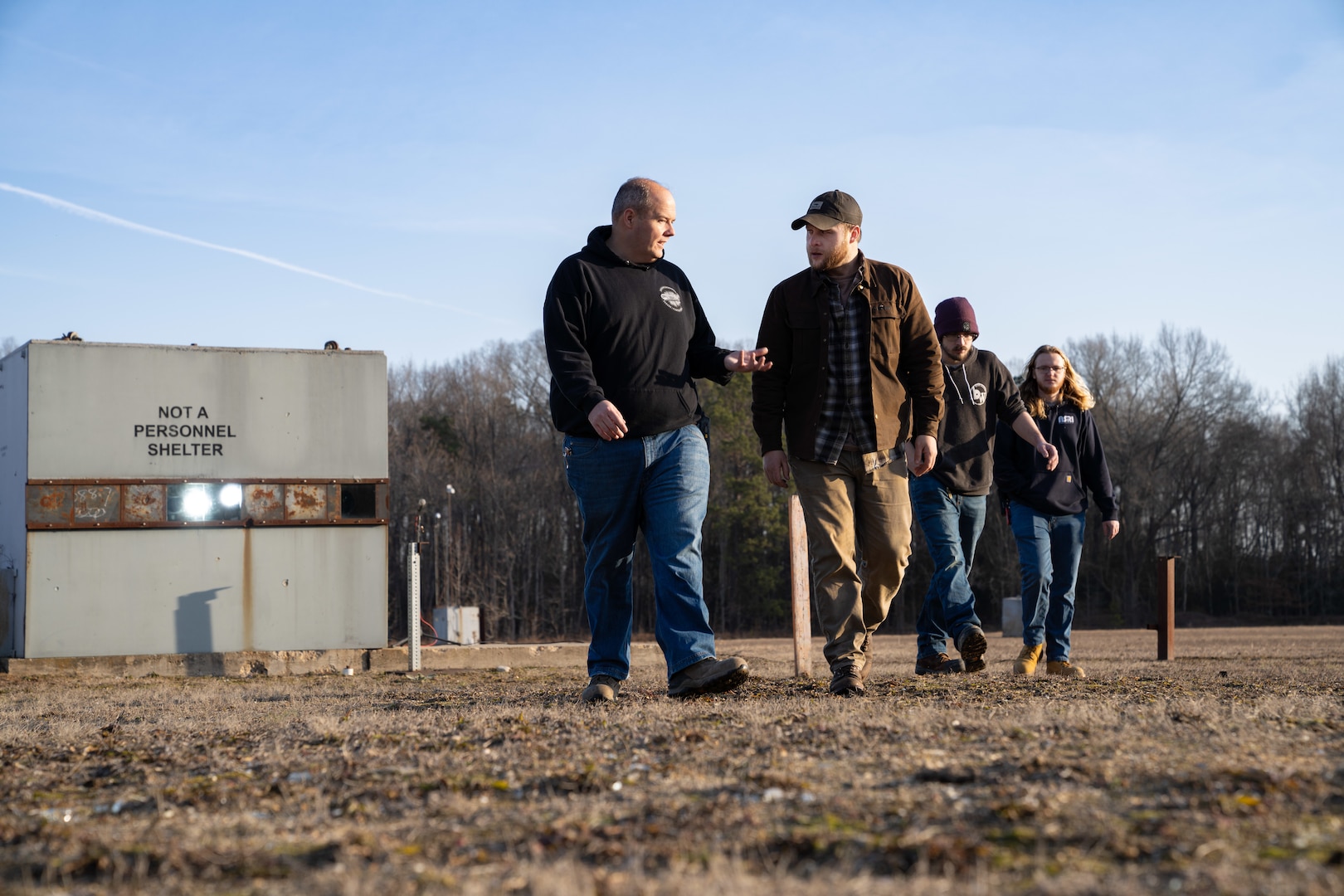 PUMPKIN NECK, Va. — Engineers and technicians of the Weapon System Test Range Operations and Data Acquisition Branch at the Naval Surface Warfare Center Dahlgren Division, Justin Stiltner, Joey Hastings, Kevin Richardson and Kurt Baumgartel, walk from the instrumentation shelter toward the gun. They are adjusting and setting up the instrumentation before a fragment impact testing event. (Dorina Watermolen/NSWCDD Photo)