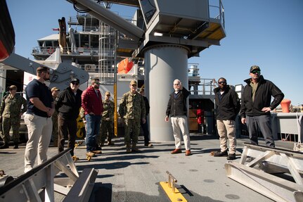 Master of Training Support Vessel (TSV) 5 Vindicator Mike Schoeller, right with hand raised, discusses the ship’s capabilities and TSV operations with Vice Adm. John Gumbleton, commander, Task Force 80 and deputy commander, U.S. Fleet Forces Command, fourth from left, during a fleet visit to Vindicator (TSV 5), assigned to Training Support Vessel Squadron (TSVRON) 4, at Naval Amphibious Base Little Creek, Va., Feb. 24, 2025.