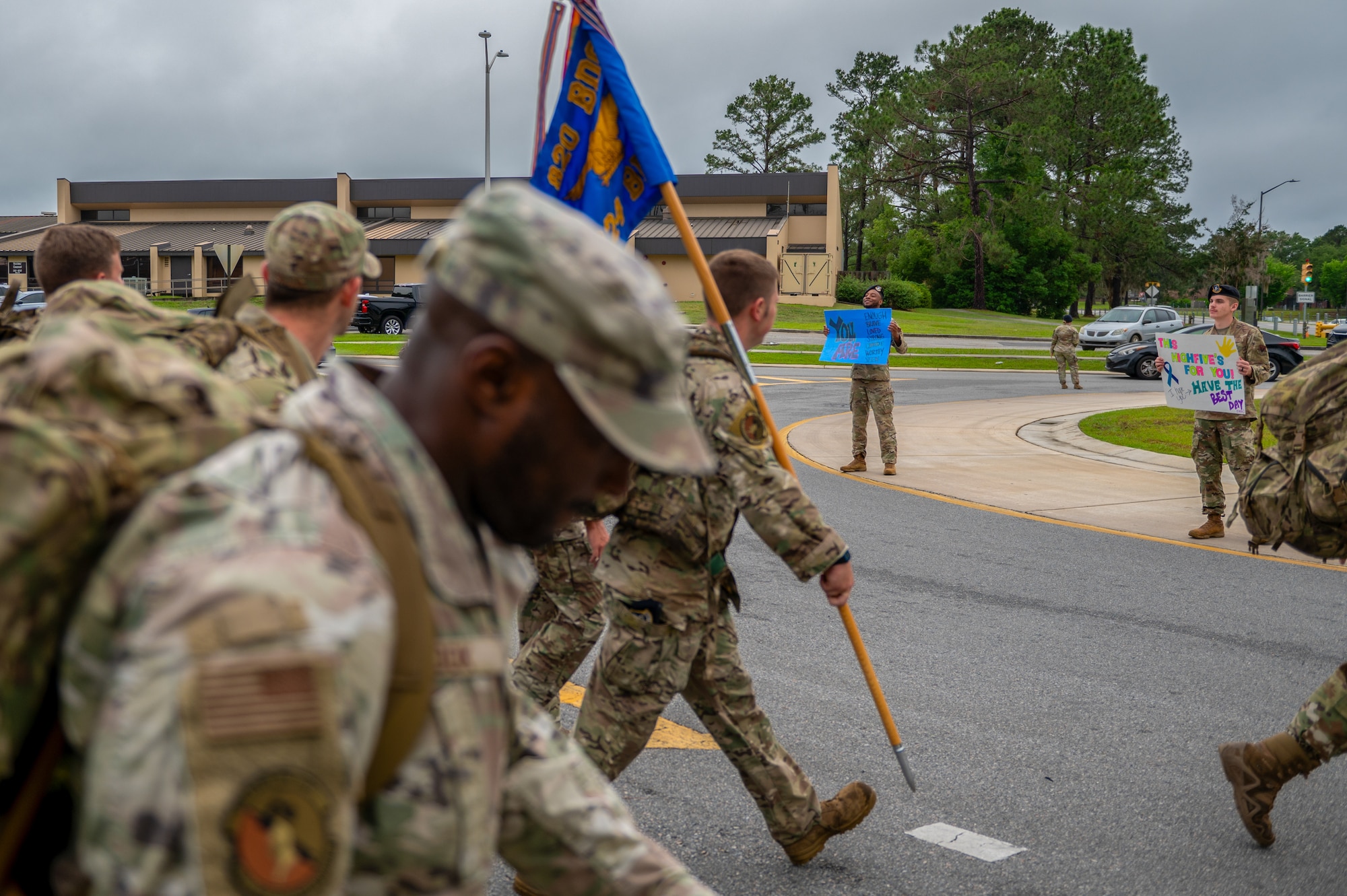 A man holding a sign is seen in the background, as a group march past.
