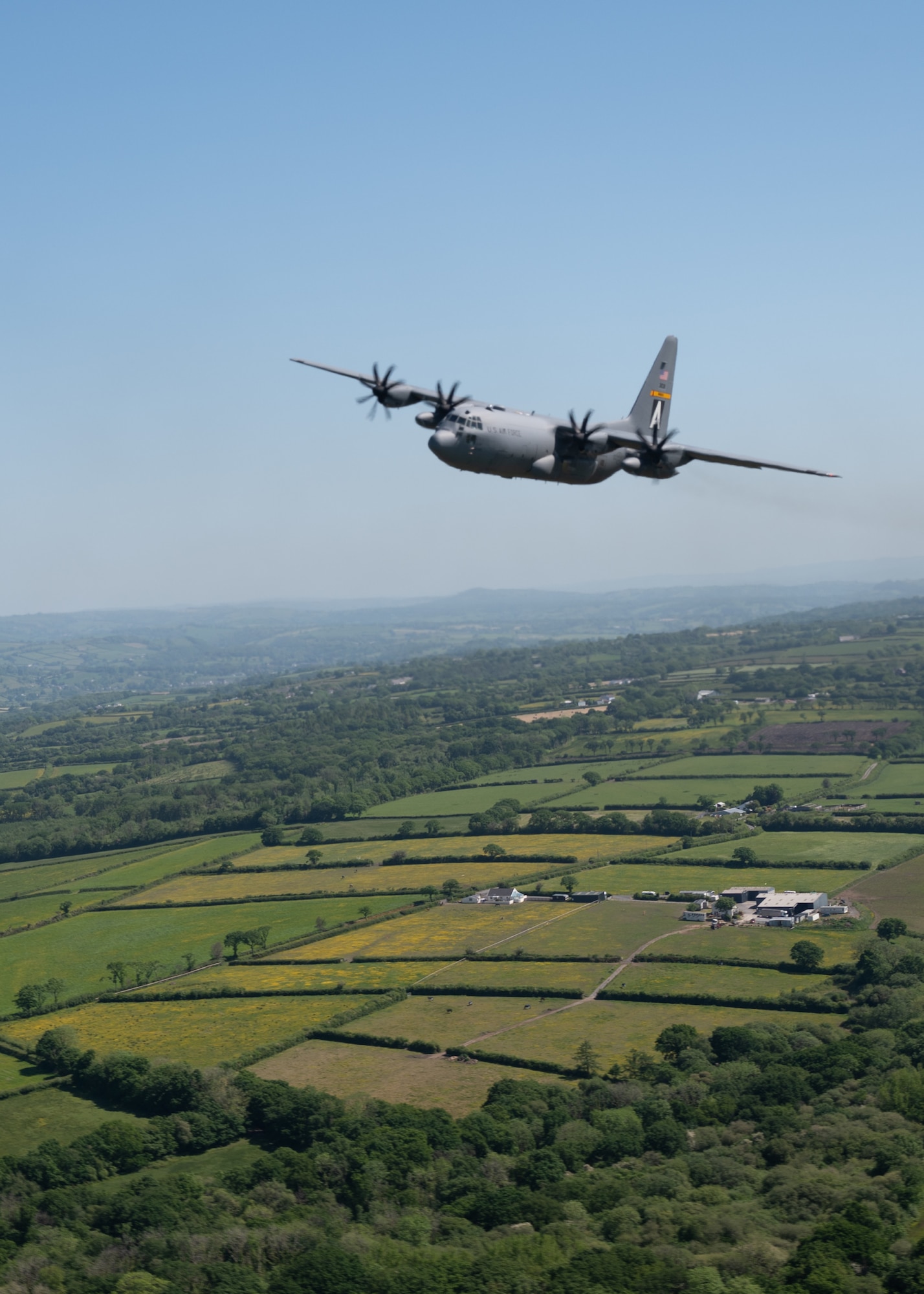 A C-130H Hercules flies over the green landscape of southern Wales,