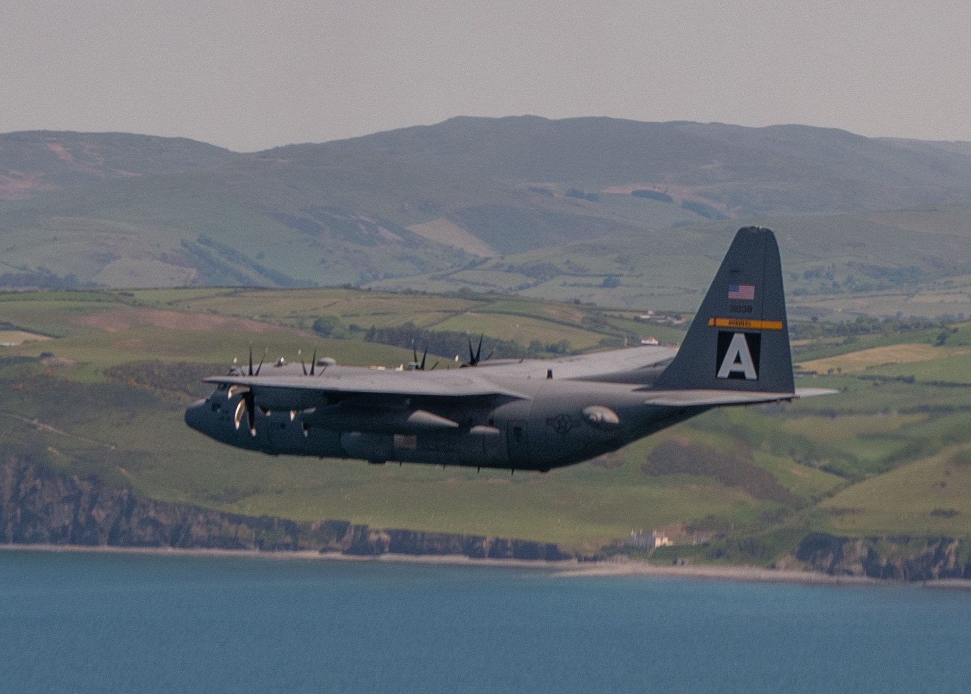 A U.S. Air Force C-130H Hercules flies over water in the United Kingdom