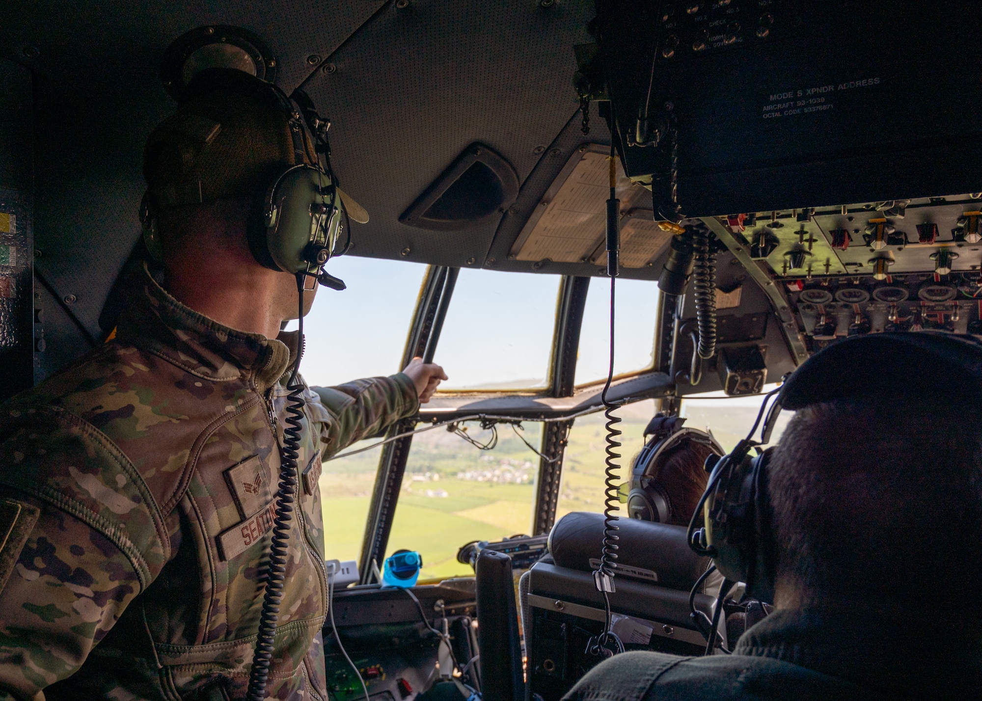 An Airman in OCPs looks out from a window on the flight deck of a C-130H