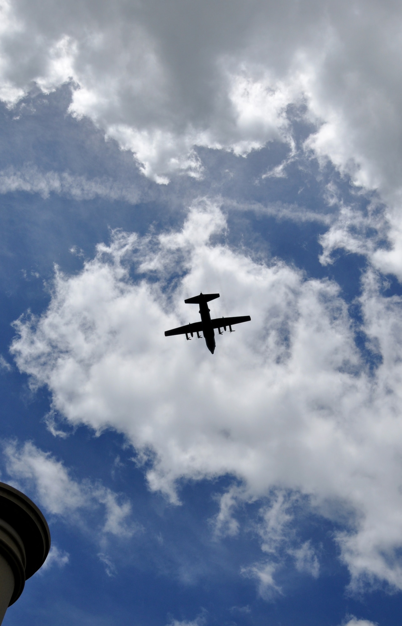 A C-130H Hercules aircraft, assigned to the 910th Airlift Wing at nearby Youngstown Air Reserve Station, Ohio, is silhouetted against the clouds above as it flies over the Veteran’s Memorial on the Triangle in Cortland, Ohio, to mark the start of the city’s Memorial Day ceremony on May 26, 2025.