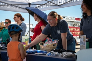 A resiliency booth volunteer gives a handout to a child during the Health Fair at Davis-Monthan Air Force Base, Arizona, May 28, 2025. The 355th Medical Group held the event to enhance operational readiness and promote physical, mental and spiritual health. (U.S. Air Force photo by Airman Samantha Melecio)
