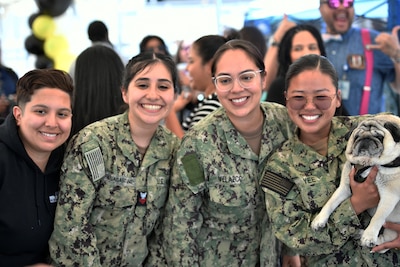 Three uniformed service members and a fourth person stand smiling and at the camera and holding a pug.