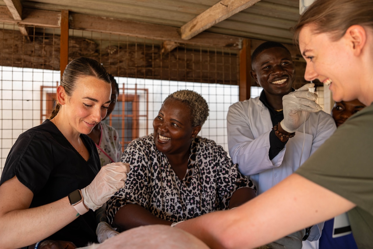 Four people smile and work on an animal wearing summer clothing and gloves.