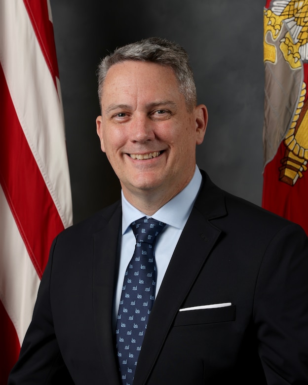 Mr. Andrew Rodgers sitting in front of U.S. and Marine Corps flags