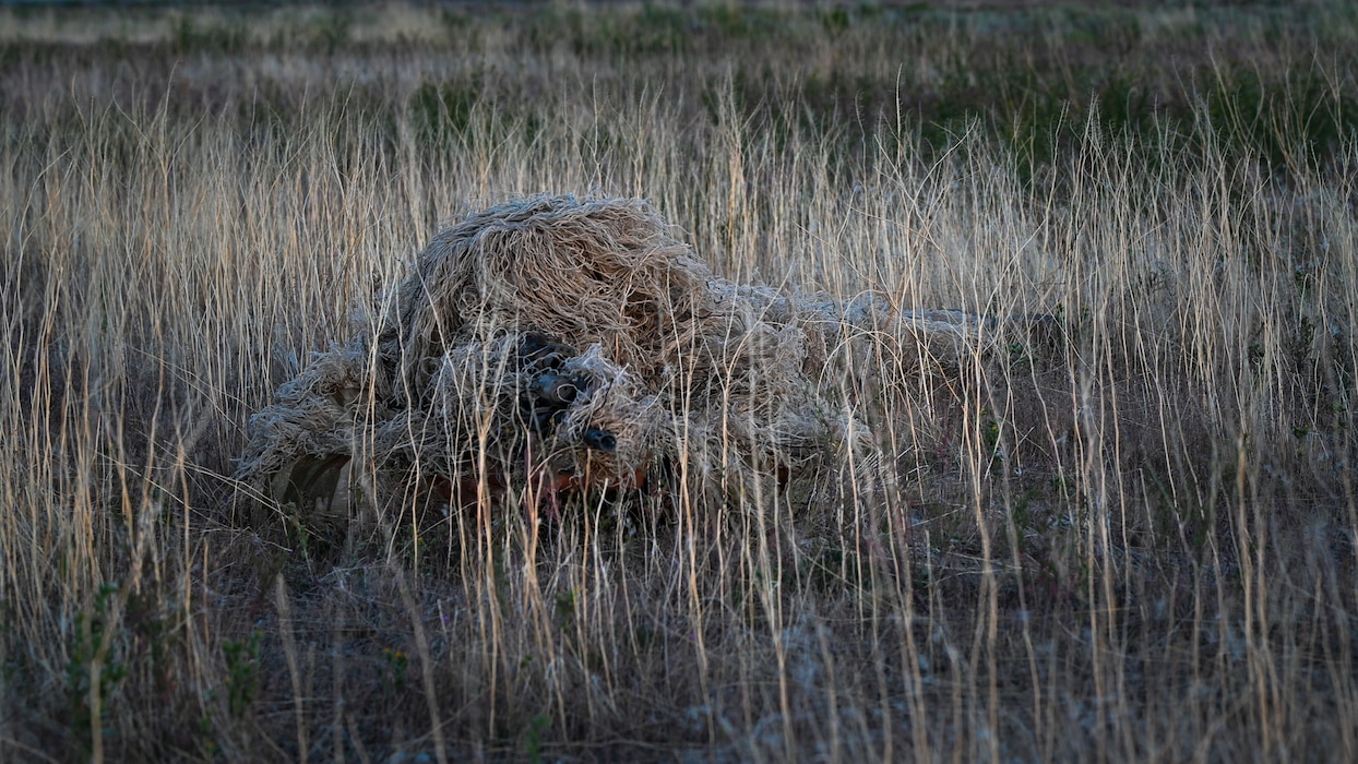 Camouflaged man aims sniper rifle