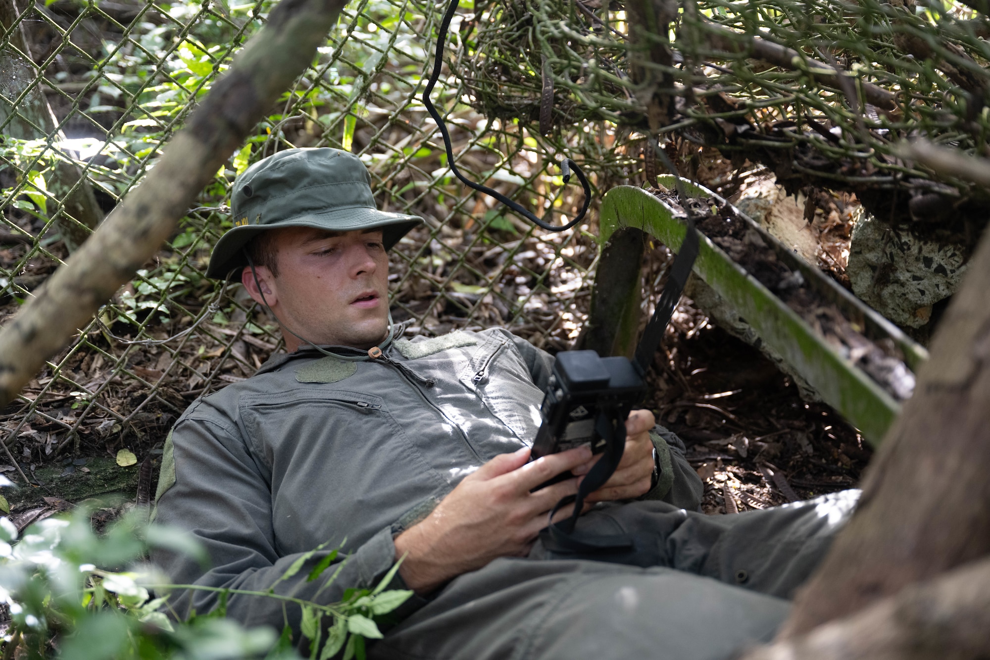 A U.S. Air Force pilot uses a handheld radio while hiding in the woods.