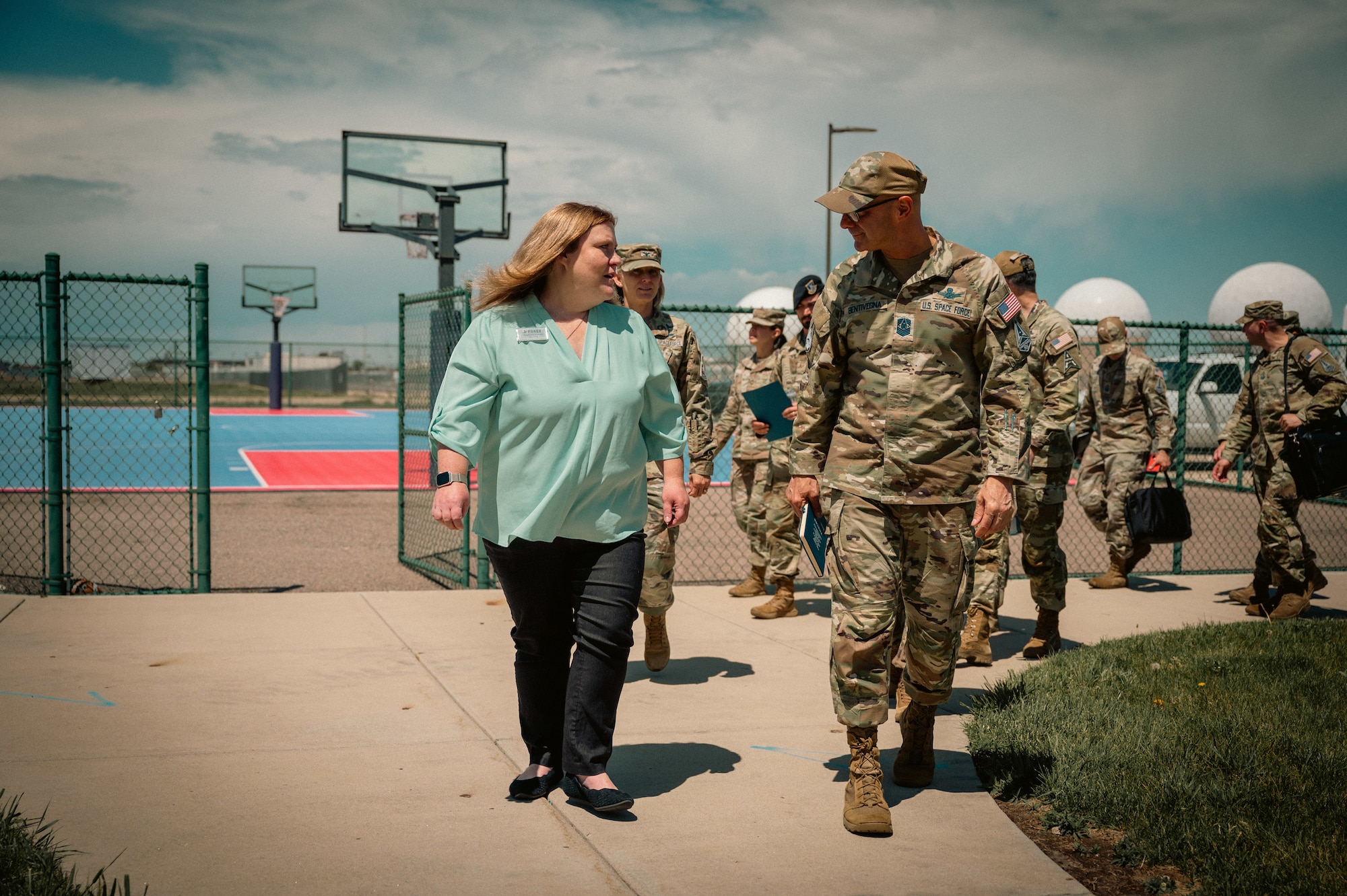 uniformed and civilian personnel walk on a sidewalk towards a building