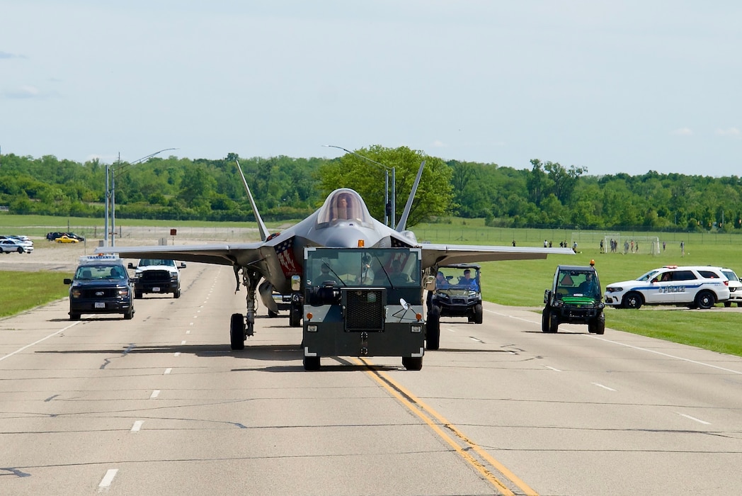 Plane on the roadway being followed by other vehicles.