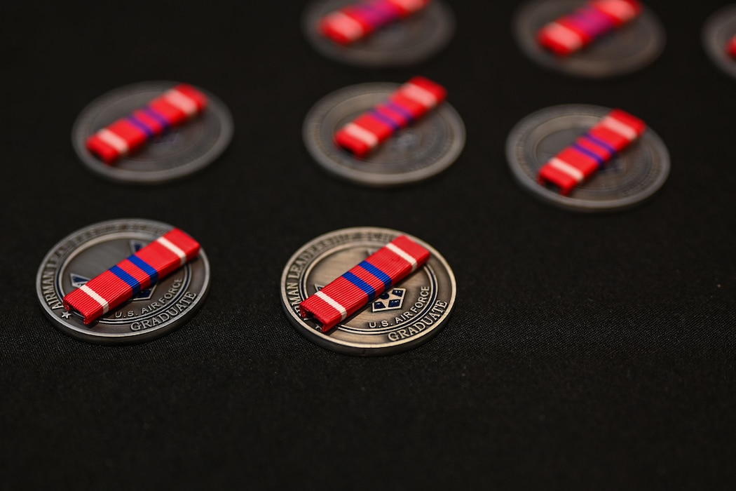 United States Air Force Noncommissioned Officer Professional Military Education Education Graduate ribbons sit on Airman Leadership coins during the Airman Leadership School Class 25-D Graduation Ceremony at the Powell Event Center, Goodfellow Air Force Base, Texas, May 22, 2025. ALS is a five-week course designed to prepare senior airmen to assume supervisory duties through instruction in leadership, followership and written and oral communication skills. (U.S. Air Force photo by Senior Airman Evelyn J. D’Errico)