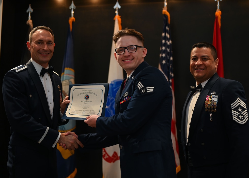 U.S. Air Force Col. Tyler Ellison, 47th Flying Training Wing commander, and Chief Master Sgt. Lester J. Largaespada, 47th Flying Training Wing command chief, present Senior Airman Tyler Daniels, 47th Operations Support Squadron air traffic control trainer, with the Airman Leadership School diploma during the ALS Class 25-D graduation at the Powell Event Center, Goodfellow Air Force Base, Texas, May 22, 2025. ALS is a five-week course designed to prepare senior airmen to assume supervisory duties through instruction in leadership, followership and written and oral communication skills. (U.S. Air Force photo by Senior Airman Evelyn J. D’Errico)