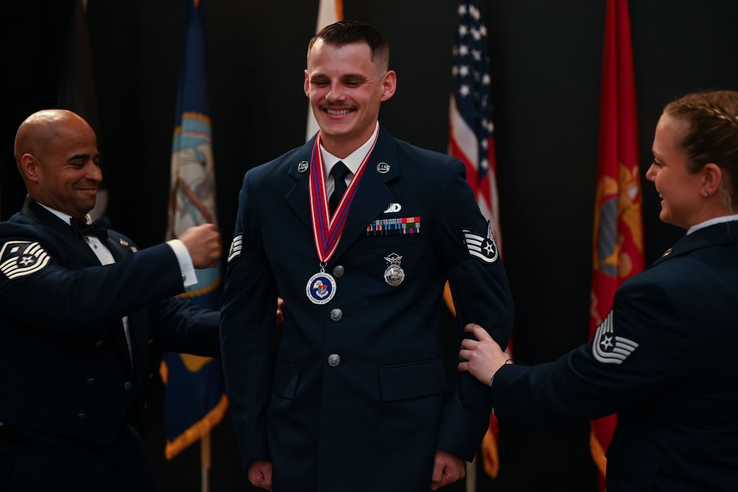 U.S. Air Force Senior Airman Joseph Orcutt, 17th Security Forces Squadron emergency communications controller, pins on the rank of staff sergeant placed on his arms by Tech. Sgt. Madyson Grace Lavender, 17th SFS flight chief, and Master Sgt. Darren Ortiz, 17th SFS first sergeant, during the ALS Class 25-D graduation at the Powell Event Center, Goodfellow Air Force Base, Texas, May 22, 2025. After graduating from ALS, airmen are eligible for promotion to staff sergeant. (U.S. Air Force photo by Senior Airman Evelyn J. D’Errico)
