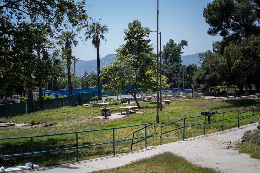 Farnsworth Park sits quiet and fenced off in Altadena, California, as crews continue wildfire debris removal May 23, 2025. The park remains closed to the public for safety as cleanup progresses, with the historic Davies Building and nearby pickleball courts visible in the distance.