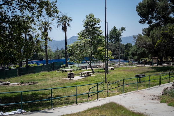Farnsworth Park sits quiet and fenced off in Altadena, California, as crews continue wildfire debris removal May 23, 2025. The park remains closed to the public for safety as cleanup progresses, with the historic Davies Building and nearby pickleball courts visible in the distance.