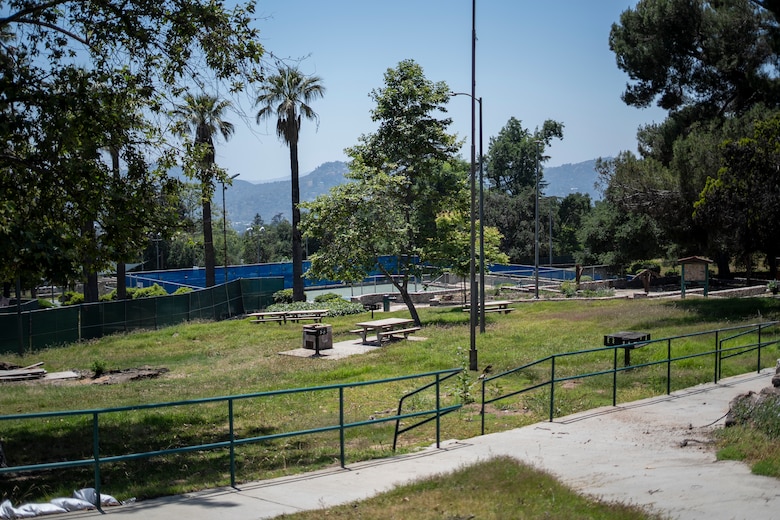 Farnsworth Park sits quiet and fenced off in Altadena, California, as crews continue wildfire debris removal May 23, 2025. The park remains closed to the public for safety as cleanup progresses, with the historic Davies Building and nearby pickleball courts visible in the distance.