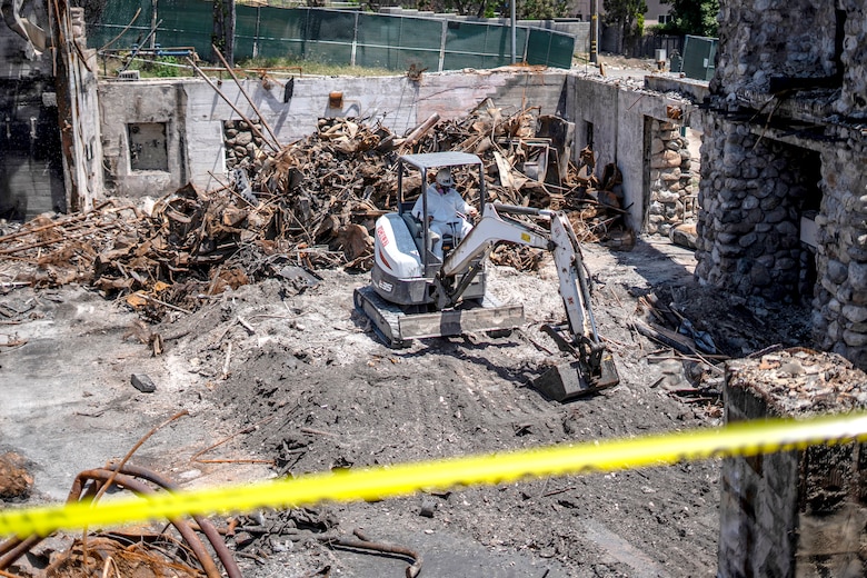 A contractor operates machinery to remove debris near the Davies Building at Farnsworth Park in Altadena, California, May 23, 2025. The structure is undergoing careful cleanup and partial preservation due to its historical significance.