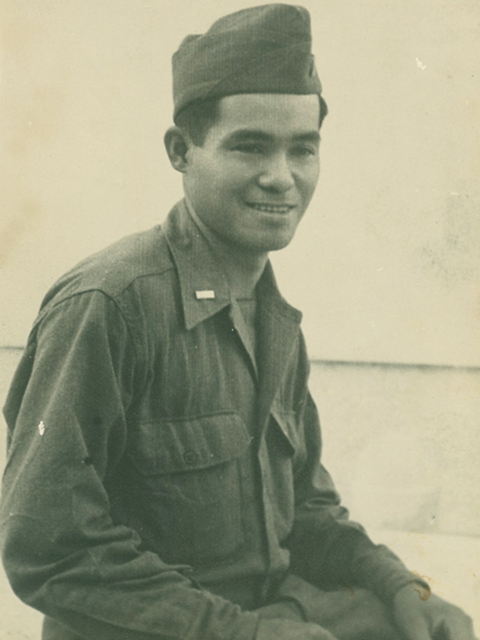 A seated man in a military uniform smiles.