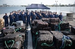 The crew of USCGC Thetis (WMEC 910) poses for a group photo behind more than 28,500 pounds of seized drugs worth more than $211 million at Port Everglades in Fort Lauderdale, Florida, May 29, 2025. The crew seized the illicit drugs in four separate interdictions during a patrol in the Eastern Pacific Ocean. (U.S. Coast Guard photo by Petty Officer 1st Class Diana Sherbs)
