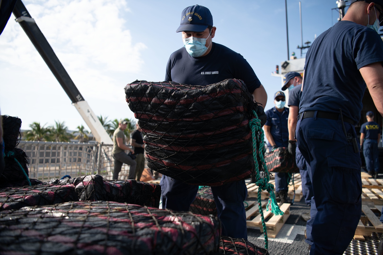 A USCGC Thetis crew member stacks a bale of cocaine on a pallet during a drug offload at Port Everglades.