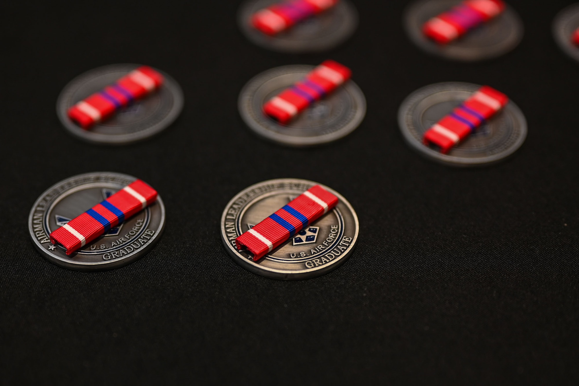United States Air Force Noncommissioned Officer Professional Military Education Education Graduate ribbons sit on Airman Leadership coins during the Airman Leadership School Class 25-D Graduation Ceremony at the Powell Event Center, Goodfellow Air Force Base, Texas, May 22, 2025. ALS is a five-week course designed to prepare senior airmen to assume supervisory duties through instruction in leadership, followership and written and oral communication skills. (U.S. Air Force photo by Senior Airman Evelyn J. D’Errico)